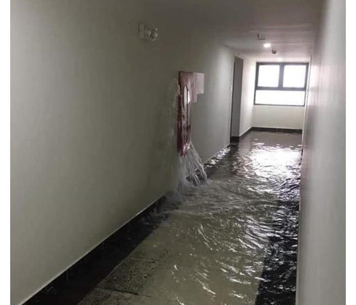 Water Leaking from wall flooding the floor of a hallway.
